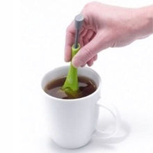 Load image into Gallery viewer, A hand holding a green tea infuser spoon over a white ceramic mug filled with tea, on a clean white background.